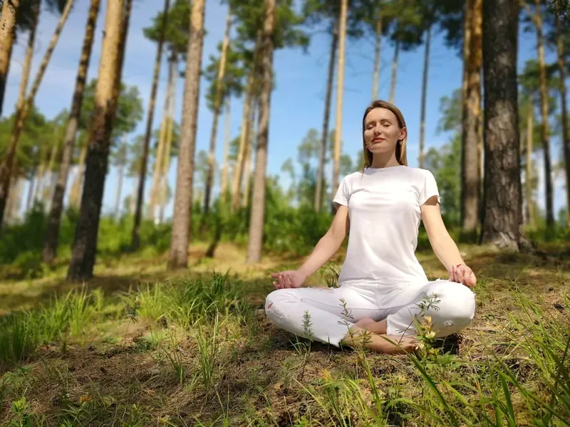 A woman sits quietly with her eyes closed on a sunlit forest floor