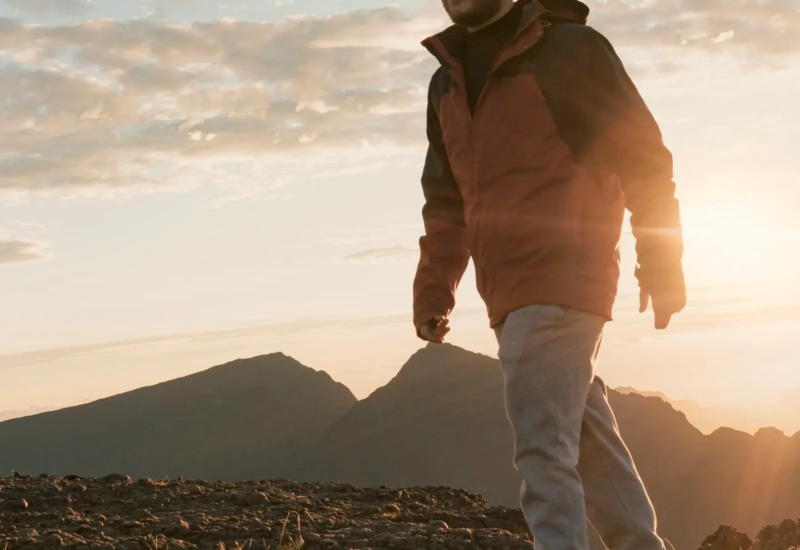A hiker walks along a rocky mountain ridge toward the low sun